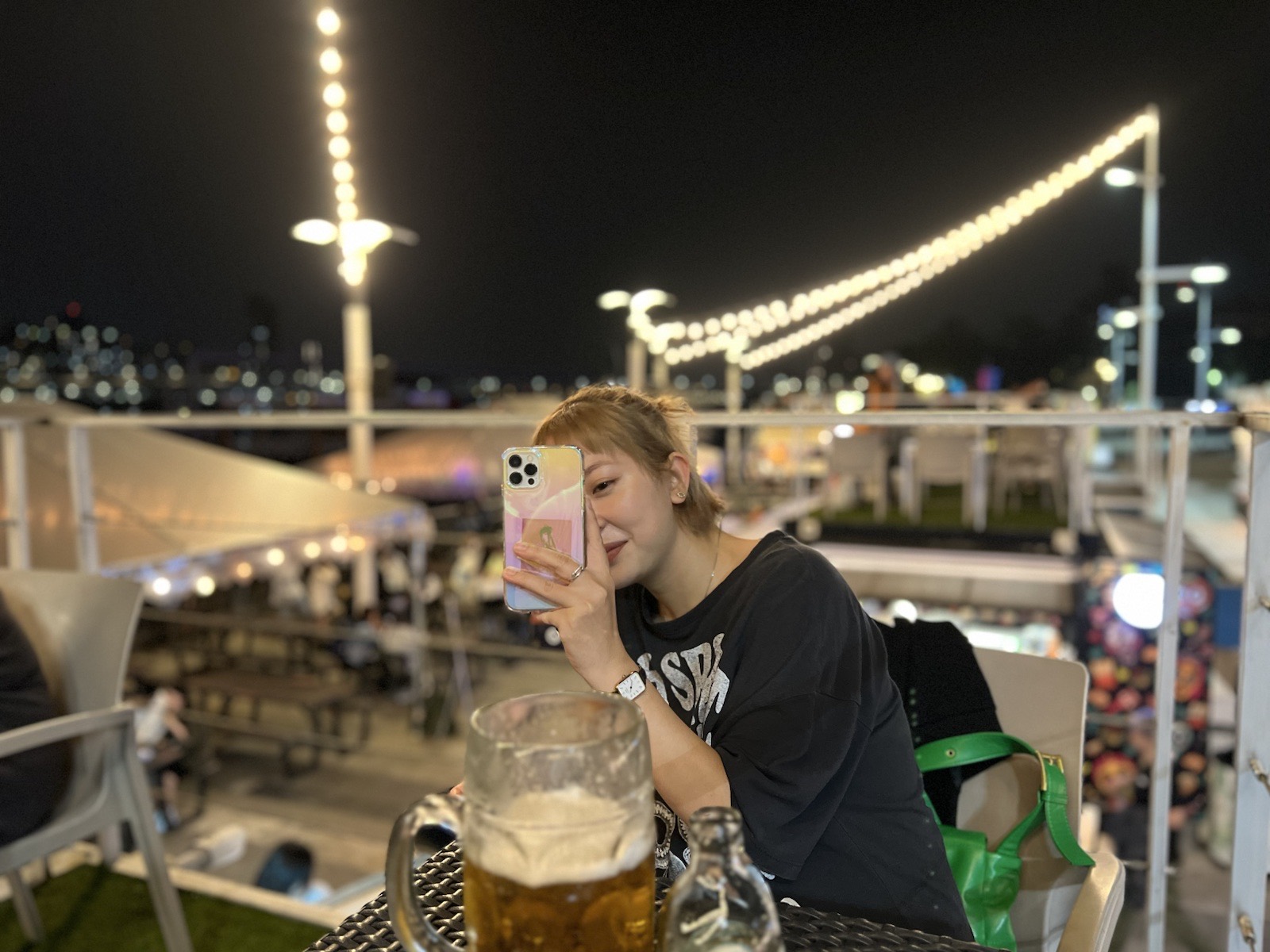 小花在大稻埕碼頭座位上拿手機拍照，桌上放著大杯啤酒